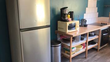 A kitchen with a stainless steel refrigerator, a microwave, a coffee maker, and wooden shelves with kitchenware.