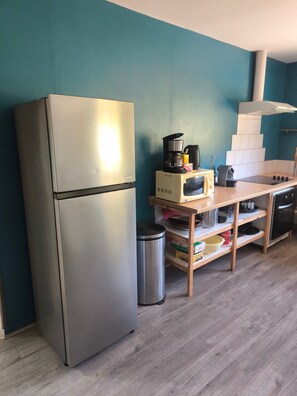 Eine Küche mit einem Edelstahl-Kühlschrank, einer Mikrowelle, einer Kaffeemaschine und Holzregalen mit Küchenutensilien.