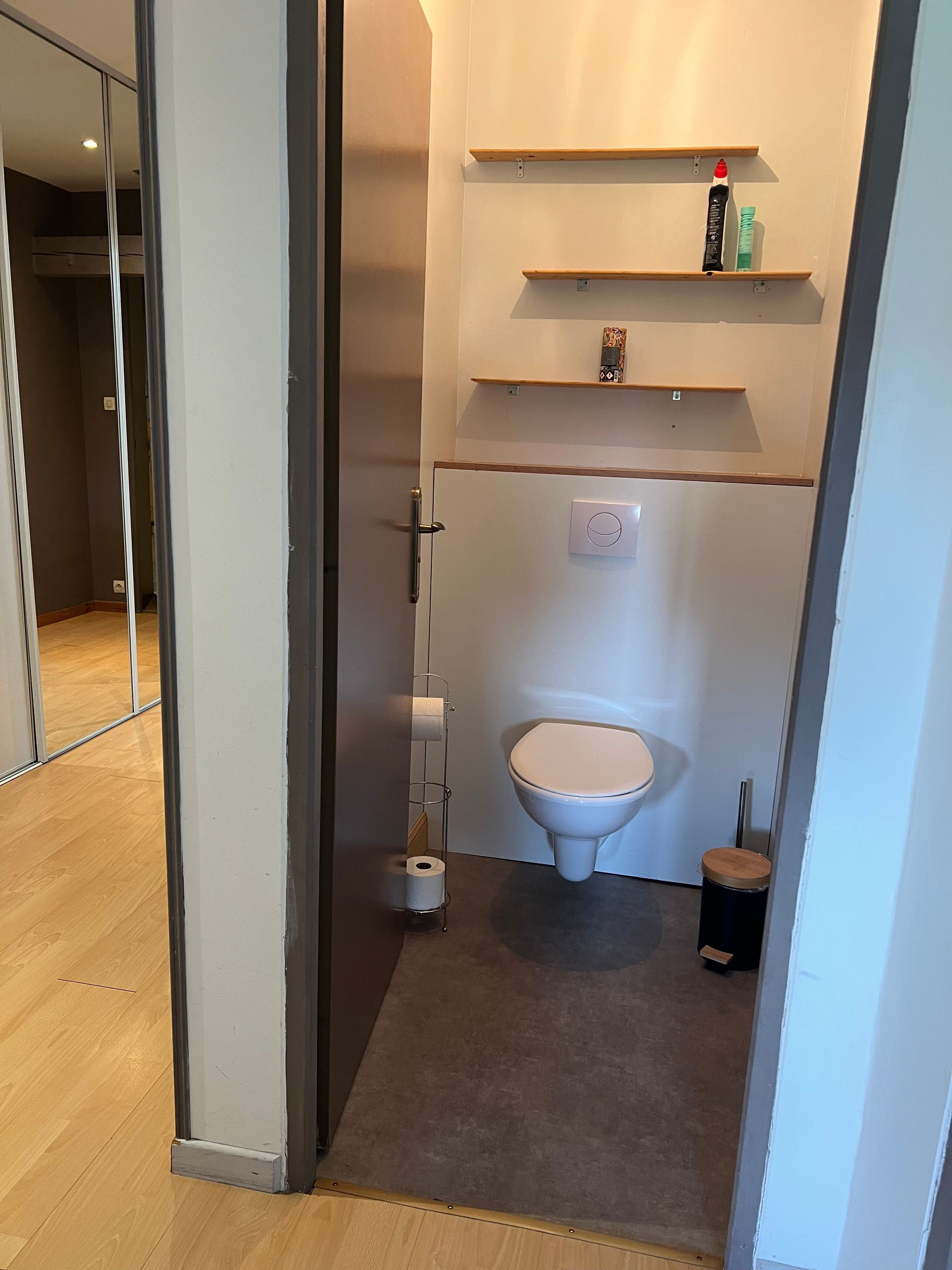 A modern bathroom with a toilet, a towel rack, and a shelf with toiletries.