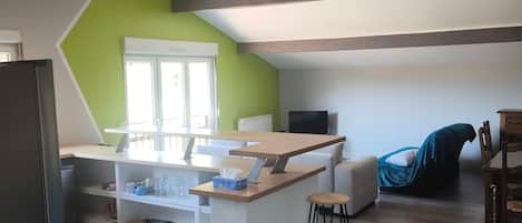 A modern kitchen with a central island, a dining area with a wooden table and chairs, and a cozy seating area with a blue chair.