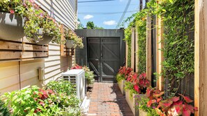 Een smal, met baksteen bestraat pad, omzoomd door weelderige beplanting en potplanten.