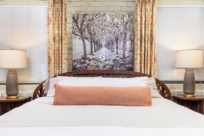 Een hotelkamer met een bed, twee nachtkastjes, een schilderij van bomen en kamergordijnen met een patroon.