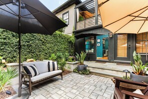 A patio with a sofa, an umbrella, and potted plants. - Hidden Garden Retreat | One-Level Near Forsyth By Lucky Savannah (Savannah)