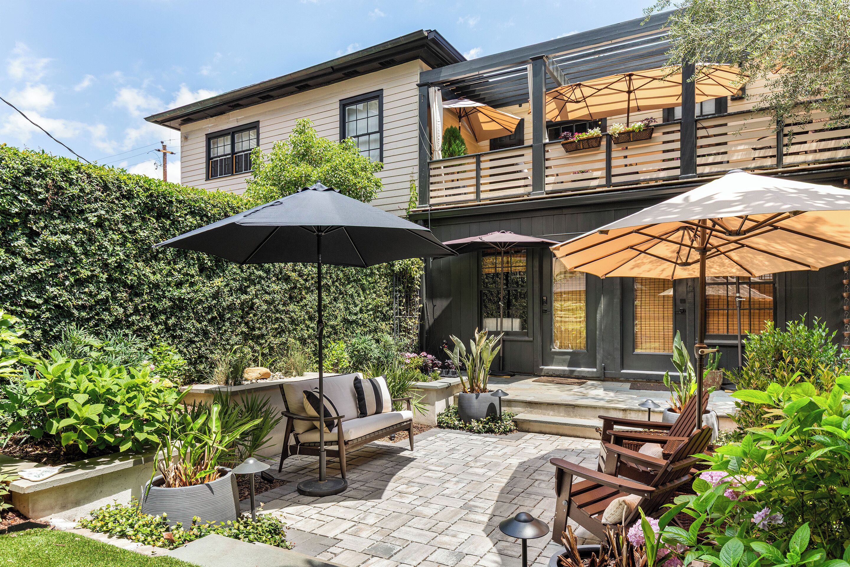 Un patio con muebles de exterior, una planta en maceta y una casa al fondo.
