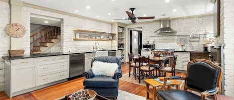 A modern kitchen with white brick walls, wooden cabinets, and a dining area with a black leather chair and wooden table.