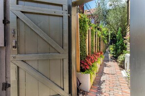 A narrow brick pathway leading to a wooden gate with a keypad lock. - Hidden Garden Retreat | One-Level Near Forsyth By Lucky Savannah (Savannah)