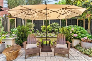 Eine Terrasse mit zwei Holzstühlen, einem gewebten Korb und einem Tisch unter einem großen Sonnenschirm.