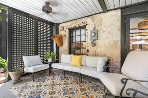 Ein gemütlicher Außenbereich mit einem weißen Sofa, zwei Sesseln, einem gemusterten Teppich und einem Blumentopf.