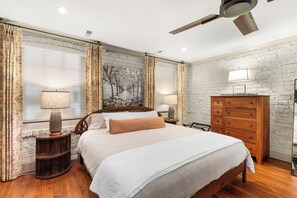 A bedroom with a wooden bed, a nightstand with a lamp, a dresser, and a ceiling fan. - Hidden Garden Retreat | One-Level Near Forsyth By Lucky Savannah (Savannah)