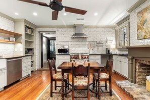Une cuisine avec une table à manger, des chaises, un ventilateur de plafond et un mur en briques.