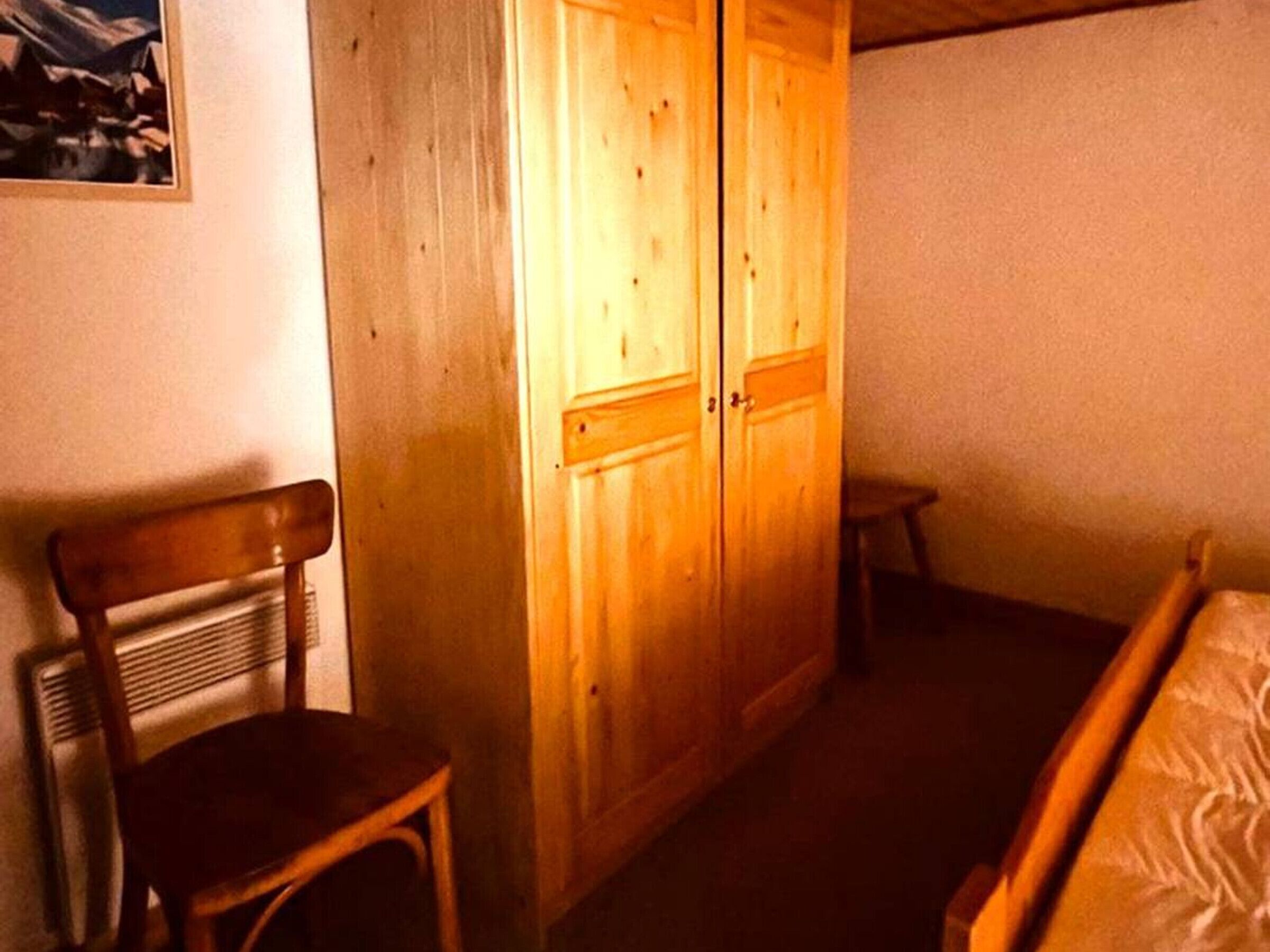 Una habitación con un armario de madera, una silla de madera y una cama.