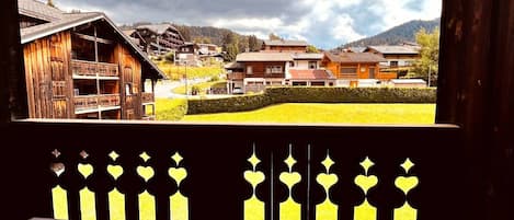 A wooden building with a balcony, a view of a village, and a mountain in the background.