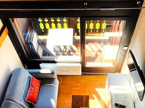 A compact living space with a sofa, a small table, and a window with a view of outdoor furniture. - Bright duplex near center - 6 guests (Les Gets)