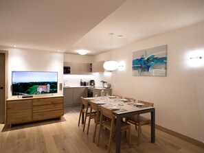 A modern dining area with a long table set for four, a television on a wooden cabinet, and a painting on the wall. - Refined apartment in Méribel center - 6 guests (Méribel)