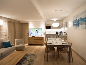A modern living room with a sofa, a TV, and a dining area with a table set for two. - Refined apartment in Méribel center - 6 guests (Méribel)