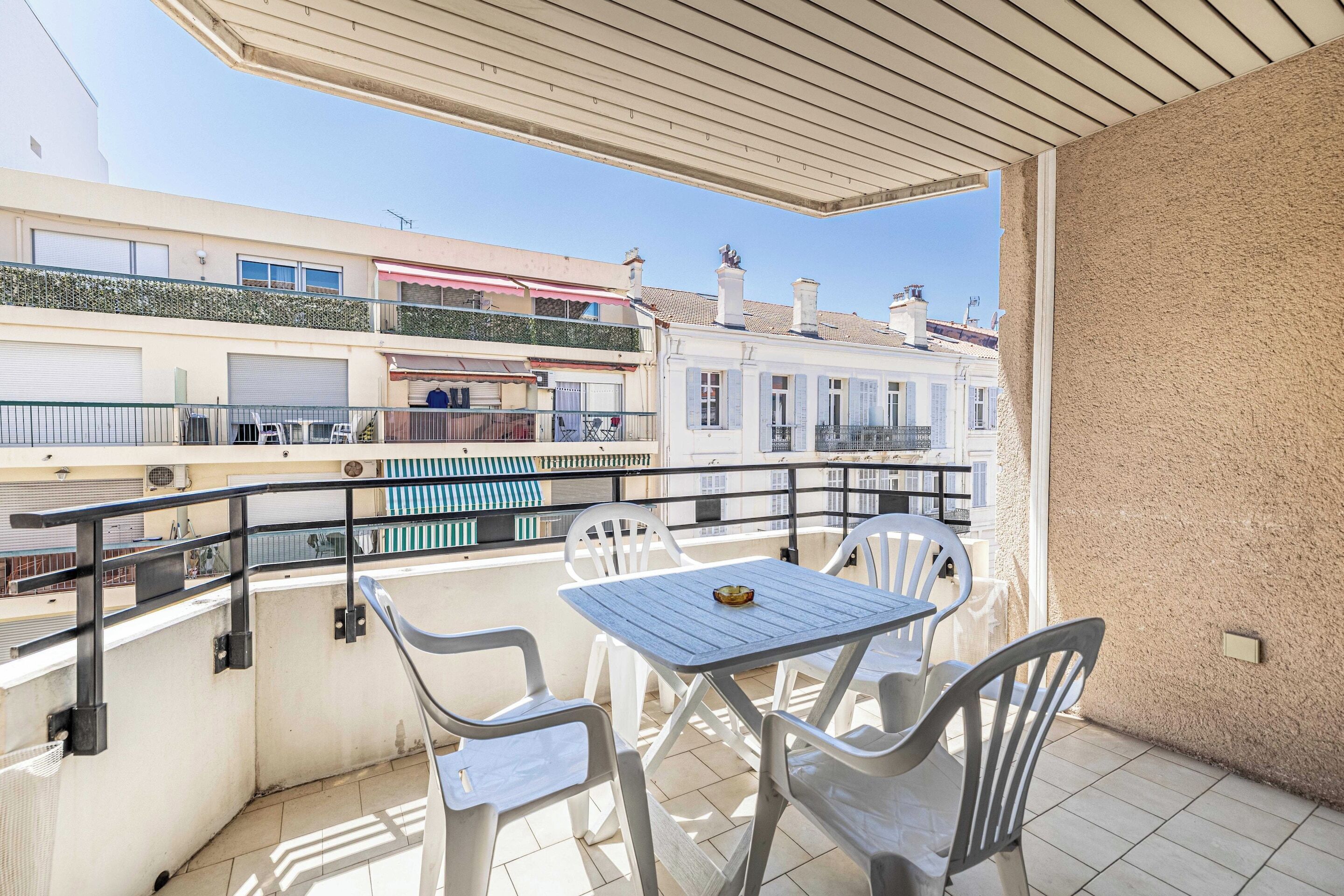 A balcony with a table and chairs, overlooking a residential area with buildings and a swimming pool.