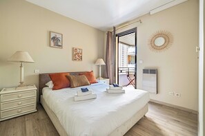 Ein Hotelzimmer mit einem Bett, Nachttischen, einem Fenster mit Vorhängen, einem Wandheizkörper und Blick nach draußen.