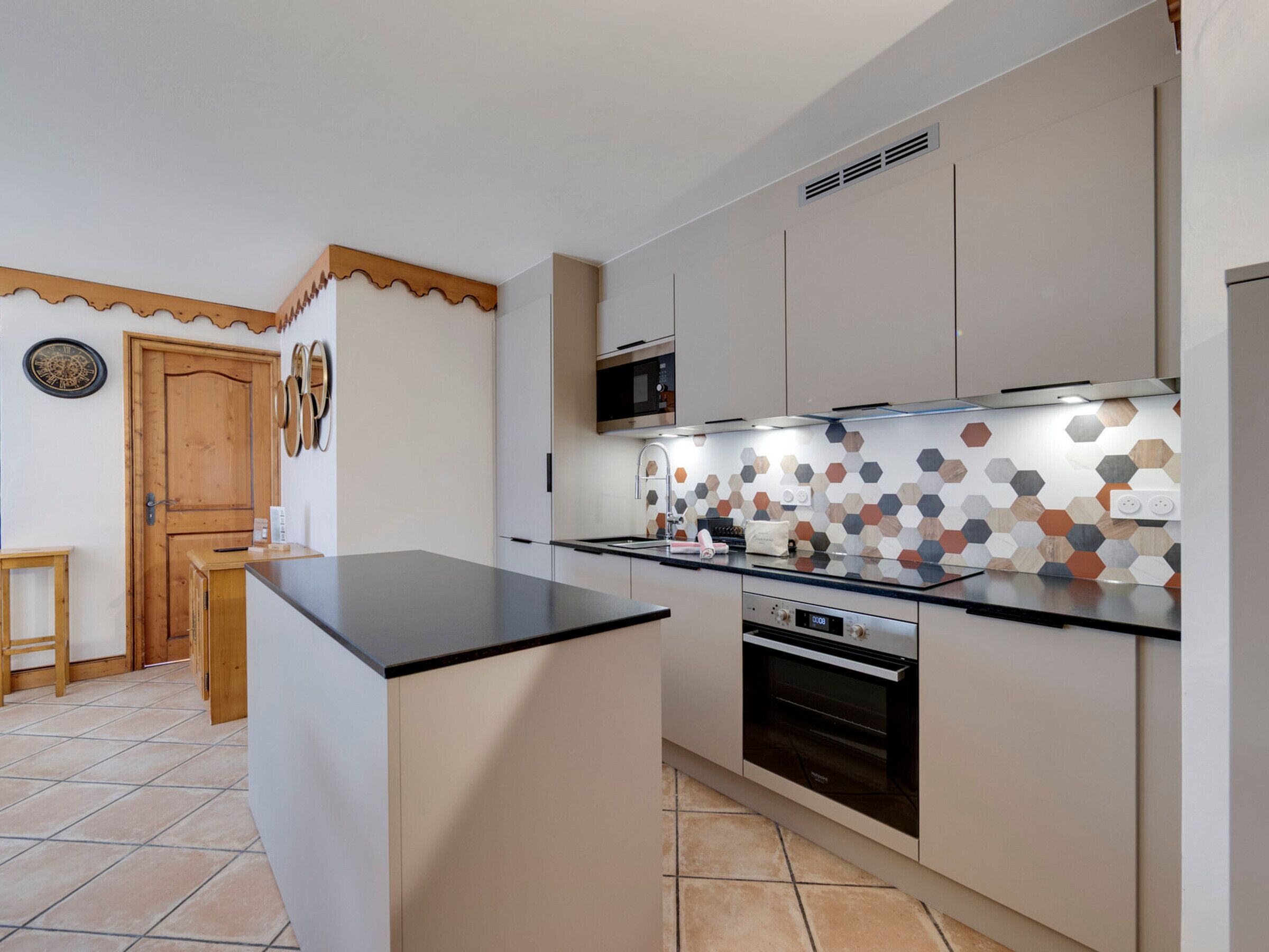 A kitchen with a central island, a microwave, oven, and a hexagonal tile backsplash.