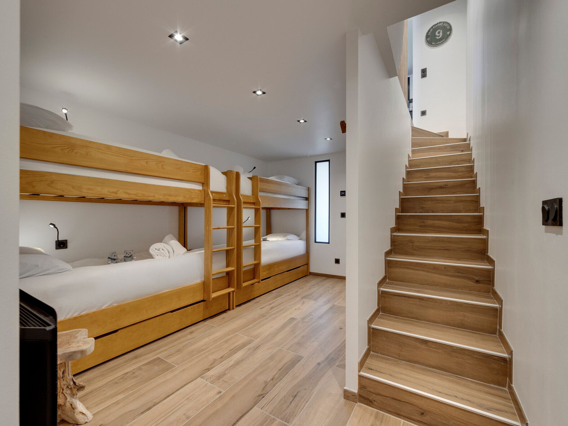 A modern hotel room with bunk beds, a wooden staircase, and a minimalist design.