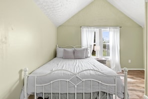 A bedroom with a single bed, a window with curtains, and a view of the outdoors.