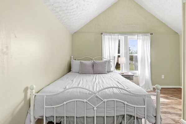 A bedroom with a single bed, a window with curtains, and a view of the outdoors.