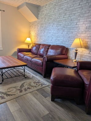 Ein gemütliches Wohnzimmer mit einem Ledersofa, einem Holztisch und zwei Lampen.