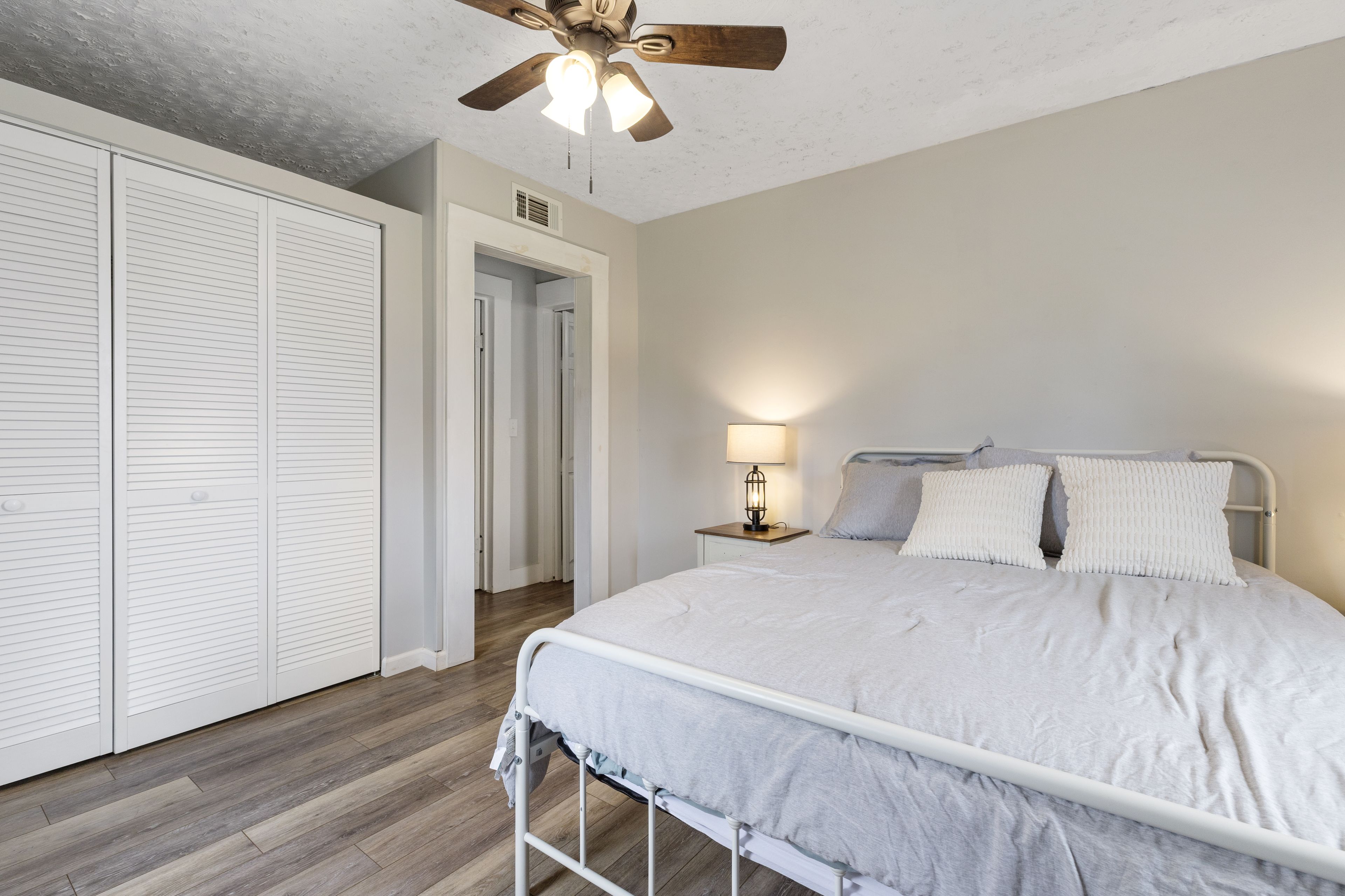 A bedroom with a bed, a nightstand, a ceiling fan, and a walk-in closet.