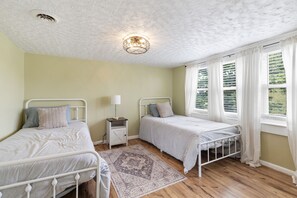 Une chambre avec deux lits simples, une table de chevet avec une lampe, un tapis à motifs et un luminaire au plafond.