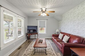 Un salon avec un ventilateur de plafond, un téléviseur, un canapé en cuir rouge et une table basse en bois.