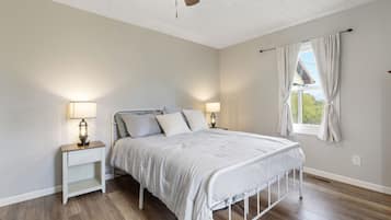 A bedroom with a bed, two bedside tables, a window with curtains, and a ceiling fan.