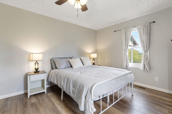 A bedroom with a bed, two bedside tables, a window with curtains, and a ceiling fan.