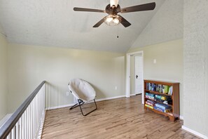 A room with a ceiling fan, a chair, and a bookshelf.