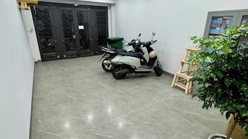 Amplio espacio interior con una moto estacionada cerca de una puerta, una planta en maceta y un estante en la pared con objetos.