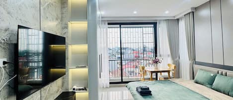 A modern bedroom with a large bed, a TV mounted on the wall, and a balcony with a view.