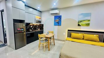 Habitación de hotel compacta con cama, una mesa de comedor con sillas, kitchenette y obras de arte en las paredes.