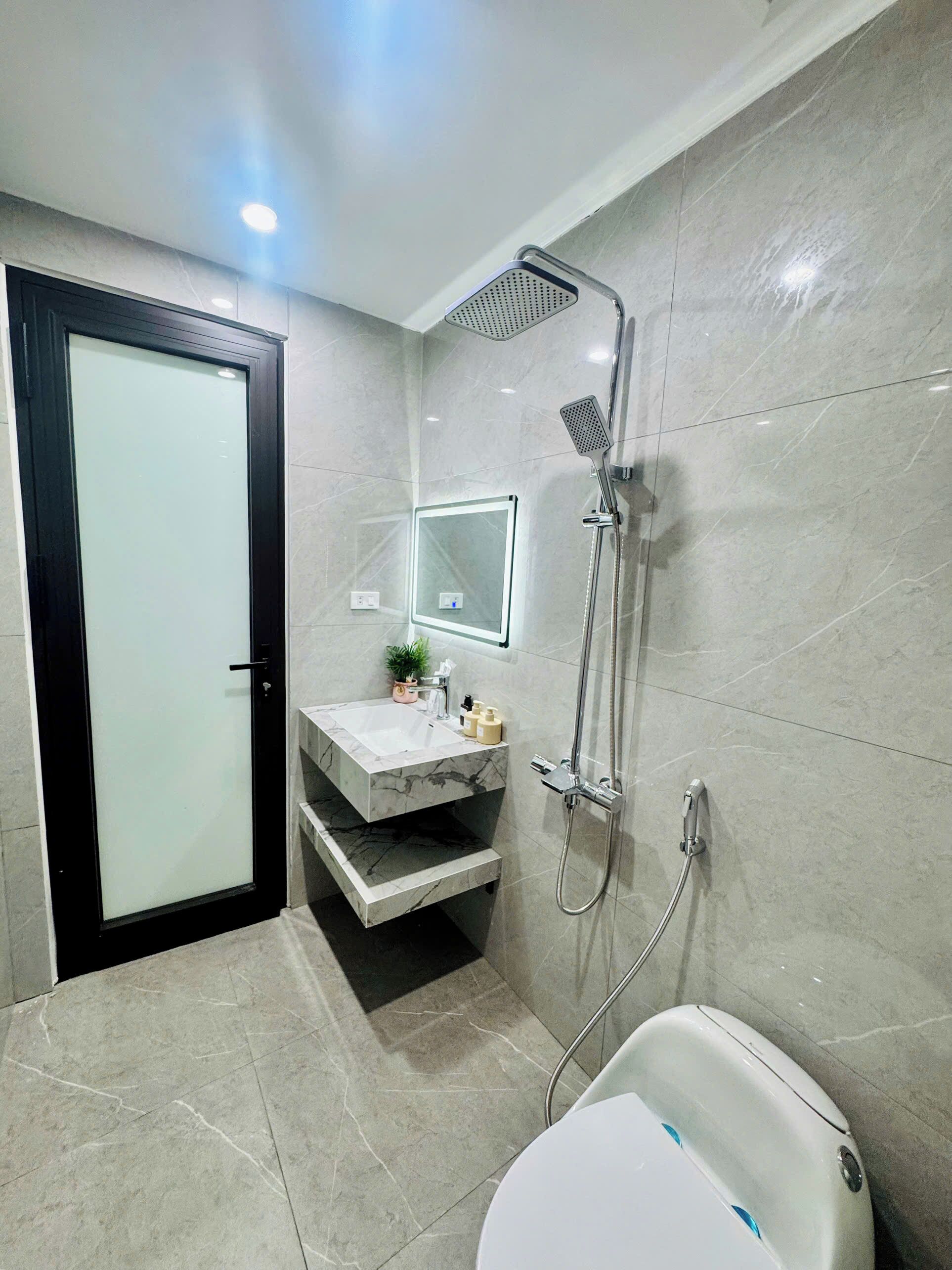 A modern bathroom with a glass door, a marble sink, a handheld showerhead, and a toilet.
