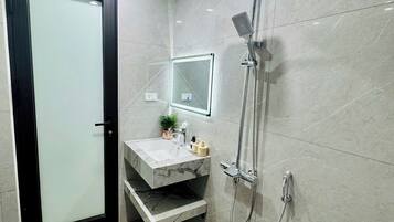A modern bathroom with a glass door, a marble sink, a handheld showerhead, and a toilet.