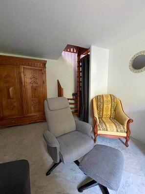 Una habitación con un sillón gris, un sillón estampado, un armario de madera y una escalera.