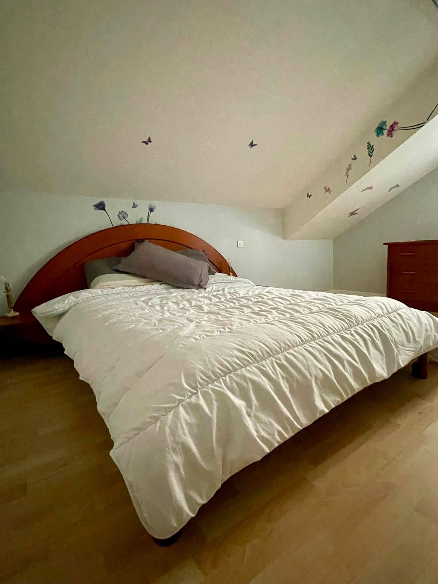 Et soveværelse med en stor seng, et træhovedgærde, en kommode og en væg med sommerfuglemotiver.