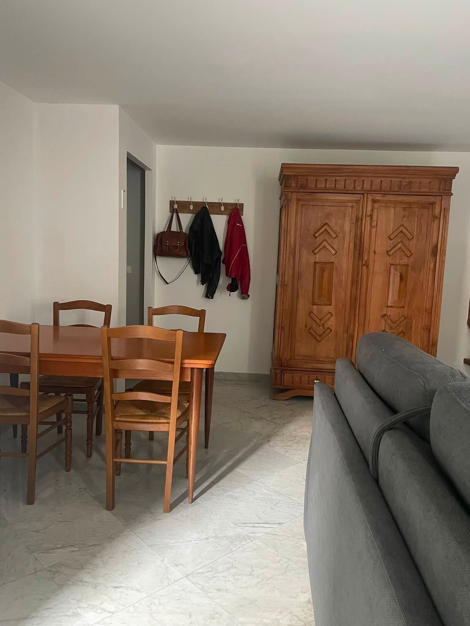 A dining area with a wooden table and chairs, a grey sofa, and a wooden wardrobe with carved doors.