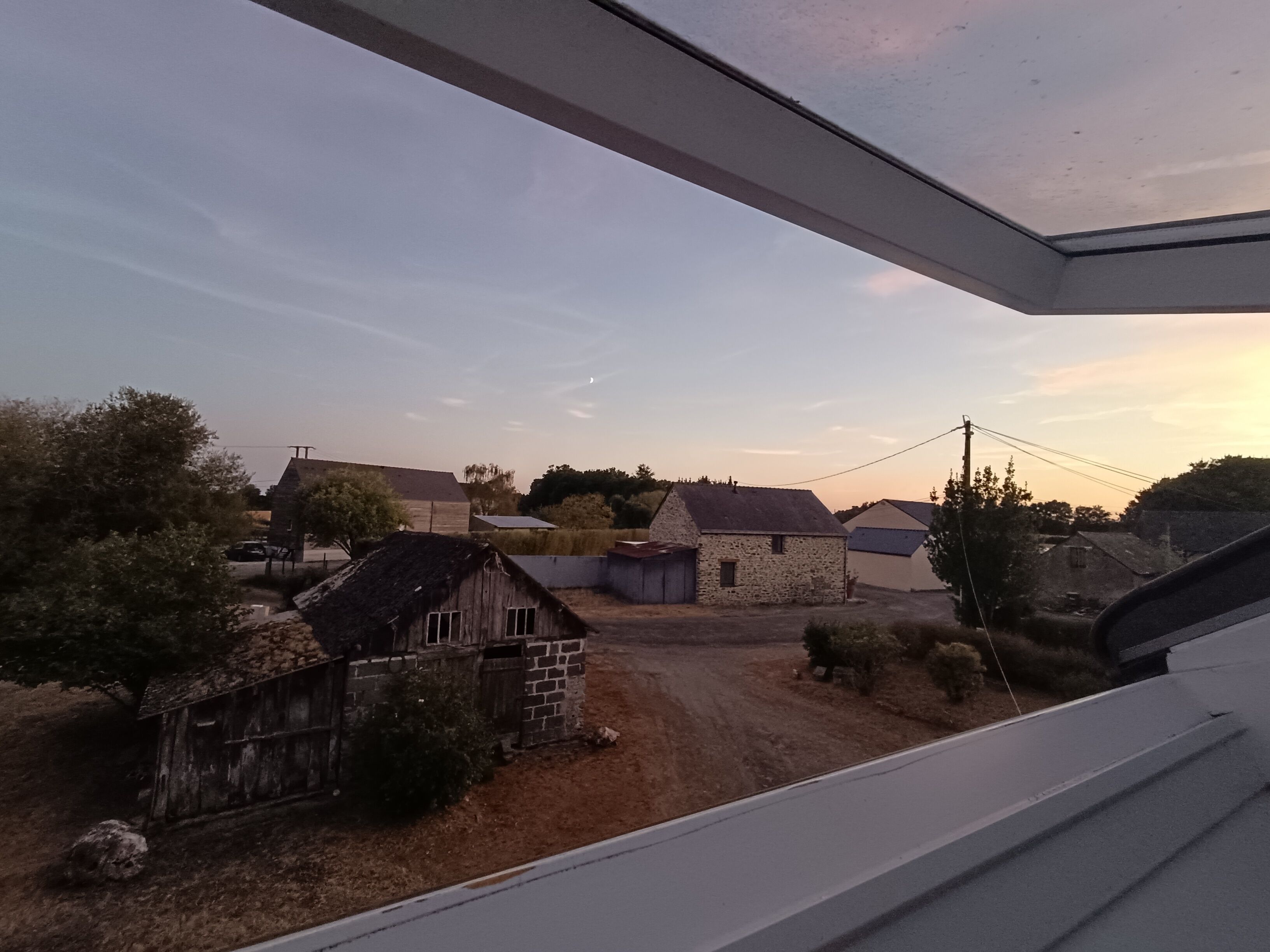 Ett lantligt landskap med stenbyggnader, en grusväg och en klar himmel.
