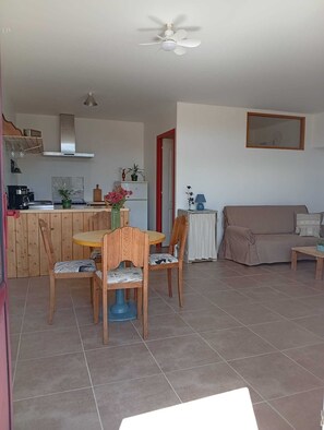 Una sala de estar con un sofá, una mesa de comedor con sillas, una zona de cocina y un ventilador de techo.