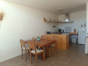 Une cuisine compacte avec une table et des chaises de salle à manger en bois, un petit îlot central doté d’un évier et un réfrigérateur blanc.