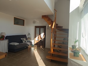 Ein Wohnzimmer mit einer Couch, einem kleinen Tisch, einer Holztreppe und einem Fenster mit Jalousien.