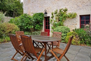Eine Terrasse im Freien mit einem runden Holztisch und vier Stühlen, umgeben von Steinmauern und Grünpflanzen.