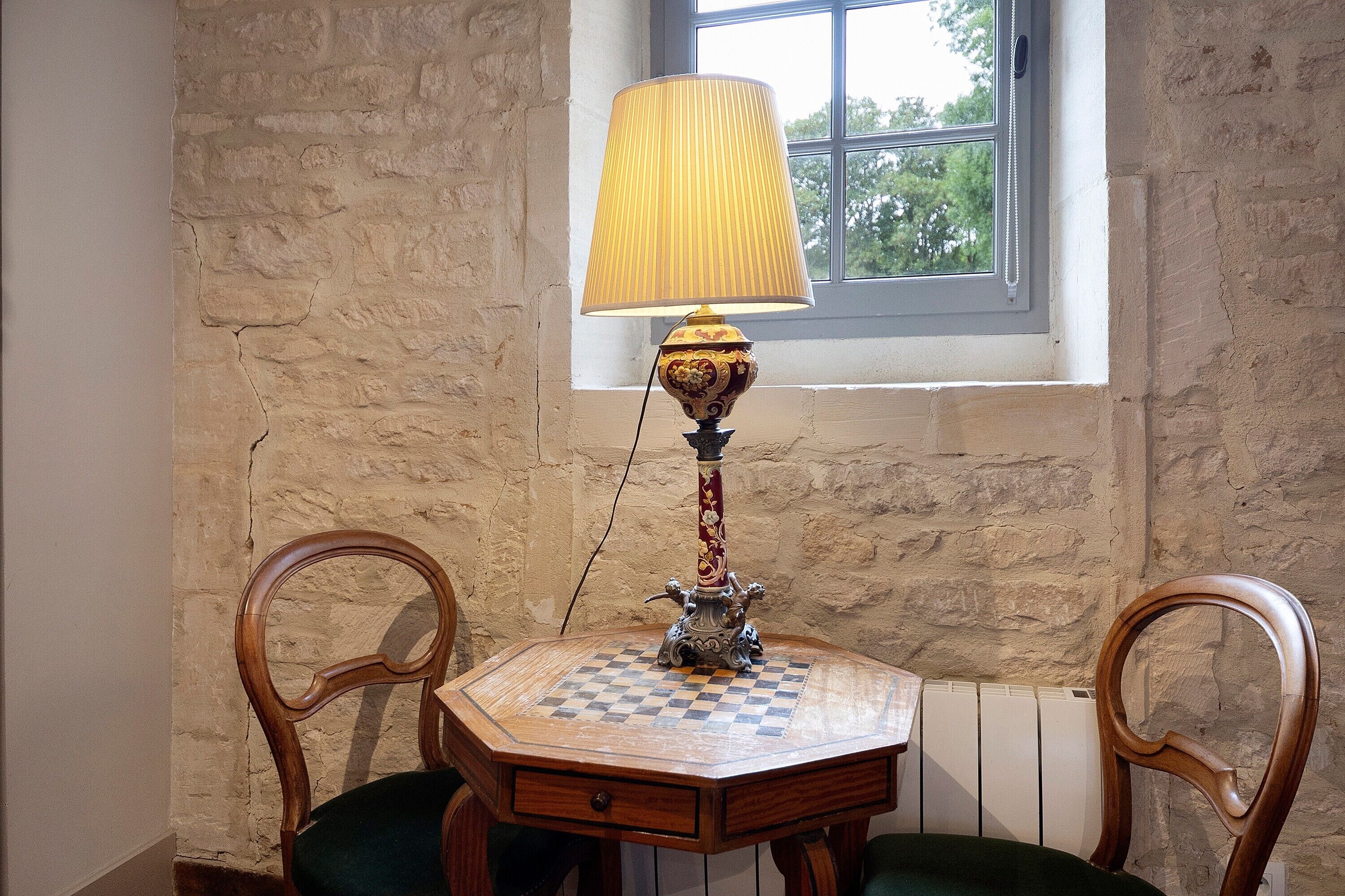Una mesa de madera con mantel a cuadros, una lámpara de pie con base decorativa y dos sillas con respaldo curvo.