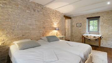 Ein Schlafzimmer mit Stehwänden, einem Bett mit weißer Bettwäsche, einem Nachttisch, einer Lampe und einem Fenster mit Blick auf Grünflächen.