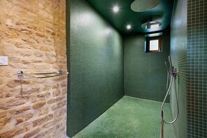 A bathroom with a stone wall, green tiled walls, a shower area, and a small window.