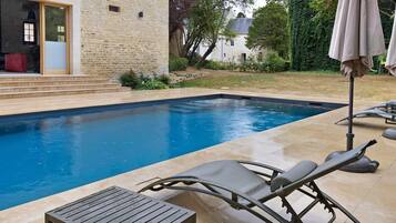 A swimming pool with a tiled deck, lounge chairs, and a covered umbrella.