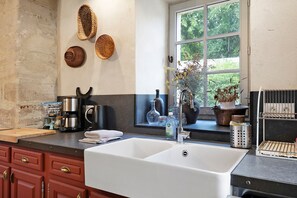 A kitchen with a large white sink, wooden cabinets, and a window with a view of trees.